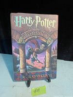Front cover of first edition Harry Potter and the Sorcerer's Stone book showing artwork with Harry Potter flying on a broomstick under archway with Hogwarts in background.