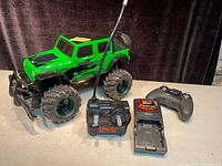 Photo showing large green Jeep Wrangler remote control toy with remote controller and battery charger on a dark background.