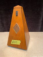 Mechanical metronome with wooden pyramid-shaped case shown front side with diamond logo.