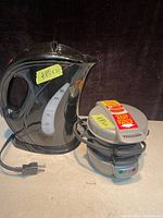 Black Salton electric kettle with water level indicator and power cord next to Salton breakfast sandwich maker with sealed label and power cord, both on black background.