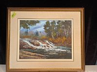 Framed oil painting of a waterfall and trees with a beige mat and gold frame.