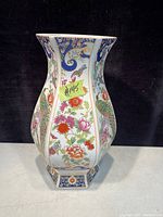 Hexagonal porcelain vase with colorful floral and peacock designs on panels, viewed front with black backdrop.