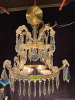 Front and partial side view of a vintage chandelier showing crystal prisms and 4 light bulbs inside.