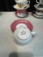 Photo showing underside of white cup and pink saucer with gold trimming and floral detailing. Marking: Royal Tudor Ware Made in England.