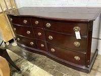 Front angle of the wooden dresser showing nine drawers with brass handles and curved front.