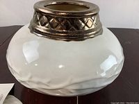 Side view of white ceramic jar with hammered texture and metallic decorative rim.