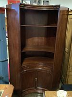 Front view of large solid wood corner cabinet with upper open shelves and lower closed storage with curved doors.