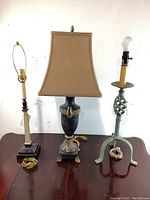 Three assorted metal table lamps on wooden surface, one with beige fabric shade and two without shades, showing varied metal bases and designs.