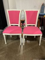 Front view of two white vintage accent chairs with pink fabric upholstery, showing their design and color.