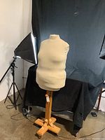 Full view of plus sized female dress form mannequin on wooden stand with wheels, beige fabric covering, natural wood base.