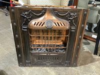Front view of vintage copper fireplace insert showing cherub decorations and metal grill with coal bed.