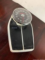 Front angle view of vintage Health-O-Meter manual platform scale showing large round dial with weight measurements up to 280 lbs and black platform surface.