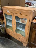 Front view of vintage wooden kitchen storage cabinet with two glass-panel doors, a top drawer, and two bottom drawers.