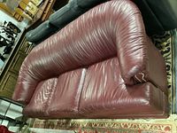 Left side angle view of vintage maroon leather couch showing overall shape, armrest details, and surface wear.