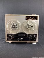 Front view of vintage reel to reel tape recorder showing tape reels, control knobs, and speaker grill.