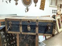 Full side view of vintage steamer trunk showing leather and metal body with rivet reinforcements, clasps and locking mechanism.