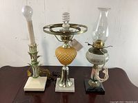 Photo of three vintage lamps showing a white ceramic lamp with green thorns, a brass and hobnail glass lamp with CFL bulb, and a white glass oil lamp with chimney.