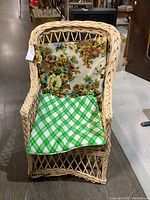 Front view of the vintage wicker chair with floral and green checkered cushions.
