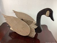 Side view of handmade wooden goose planter showing the carved wings and hollow back planter section, black head and beige wooden body.