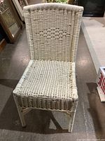 Front view of used white wicker accent chair on a concrete floor showing woven seat and decorative back.
