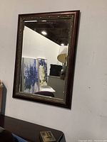 Full shot of the rectangular wooden framed mirror hanging on a wall showing its size and reflective glass surface.