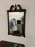 Front side view of the wooden mirror showing the ornate carved top and clear mirror glass.