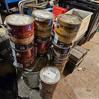Photo of stacked paint cans showing Sherwin Williams SuperDeck and WoodScapes exterior semi-transparent deck stains in various brown/rust colors.