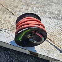 Red Snap-on air hose coiled on black retractable reel with metal mounting bracket, shows wear and dirt, view from side.