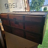 Closed view of the antique cedar chest highlighting wood grain, metal straps, latch, and overall exterior condition.
