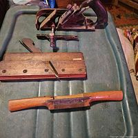 Three antique hand tools on green textured surface: Stanley No. 78 brush plane, wooden molding plane, and brass inlaid spoke shave.