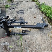 Thule branded black metal bike carrier lying on the ground showing the hitch attachment and securing straps.