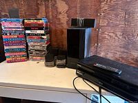 Samsung Blu-ray player with remote control, black subwoofer and satellite speakers visible on table with plywood wall background.