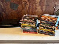 Photo of black Sony Blu-ray/DVD player with two stacks of DVDs including children's and family titles.