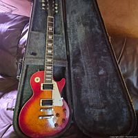 Full view of guitar in open hard shell case showing body, neck and plush interior