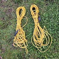 Two yellow extension cords coiled and placed on grass, each about 60 feet long, showing visible signs of use and some dirt marks.