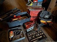 Photo showing the full assortment of tools in the lot including power tool jigsaw, hand saw, socket set, toolbox, and tool bag on wooden floor.