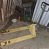 Yellow hydraulic pallet jack with chipped paint and forks visible on concrete floor