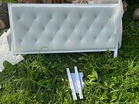 Full view of white PU leather tufted headboard lying on grass with two metal mounting brackets beneath it.