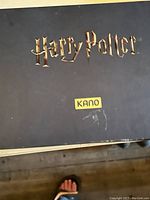 Black box lid with gold Harry Potter and Kano logos on wood floor