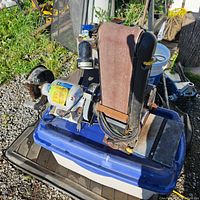 Stationary belt and disc sander placed on a blue base, showing sanding belt and disc, motor, and power cords in a workshop setting.
