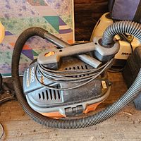 Photo of Ridgid wet/dry shop vac with black and orange plastic body, coiled hose on top, carry handle and vent slots visible.