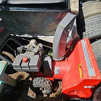 Side view showing red steel auger housing with model marking 8/25, grey discharge chute, gas tank and front wheel