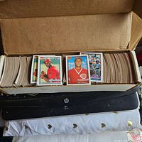 Photo of a large collection of baseball cards neatly organized in a long cardboard box with several cards visible on top, featuring players in baseball uniforms.