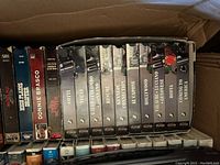 Box of VHS tapes, mix of drama and action movies such as 'Donnie Brasco' and 'The Rescuers'