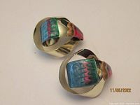 Pair of clip-on art earrings with a colorful painted panel in blue, white, pink and green colors on a metallic base, with a wavy design and clip-on back.