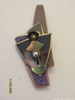 Full view of the artisan brooch showing its layered geometric shapes and mixed metal colors.