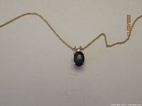 Blue sapphire oval pendant on 14k gold chain laid out flat on white background