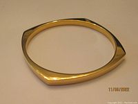 Gold tone rigid bracelet photographed from a top angle showing its slightly angular shape and smooth polished surface.