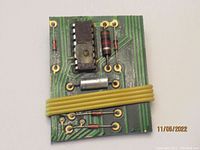 Front view of vintage computer chip brooch showing integrated circuit and electronic components with a yellow wire wrapped around it
