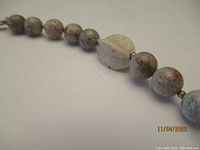 Close-up view of round stone beads showing natural jasper and riverstone textures spaced with small gold beads.